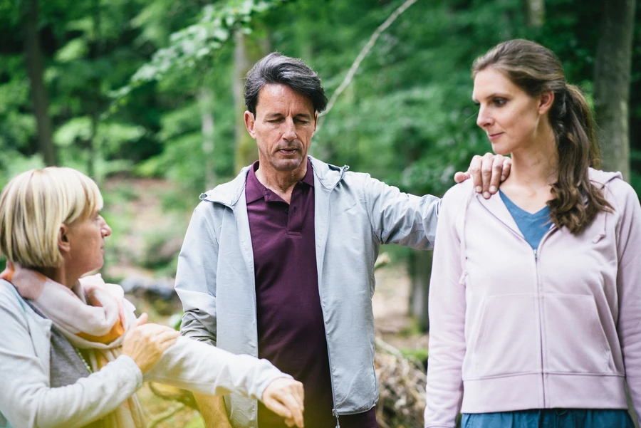 Mann steht mit geschlossenen augen drau&szlig;en mit zwei frauen und h&auml;lt sich an ihnen fest